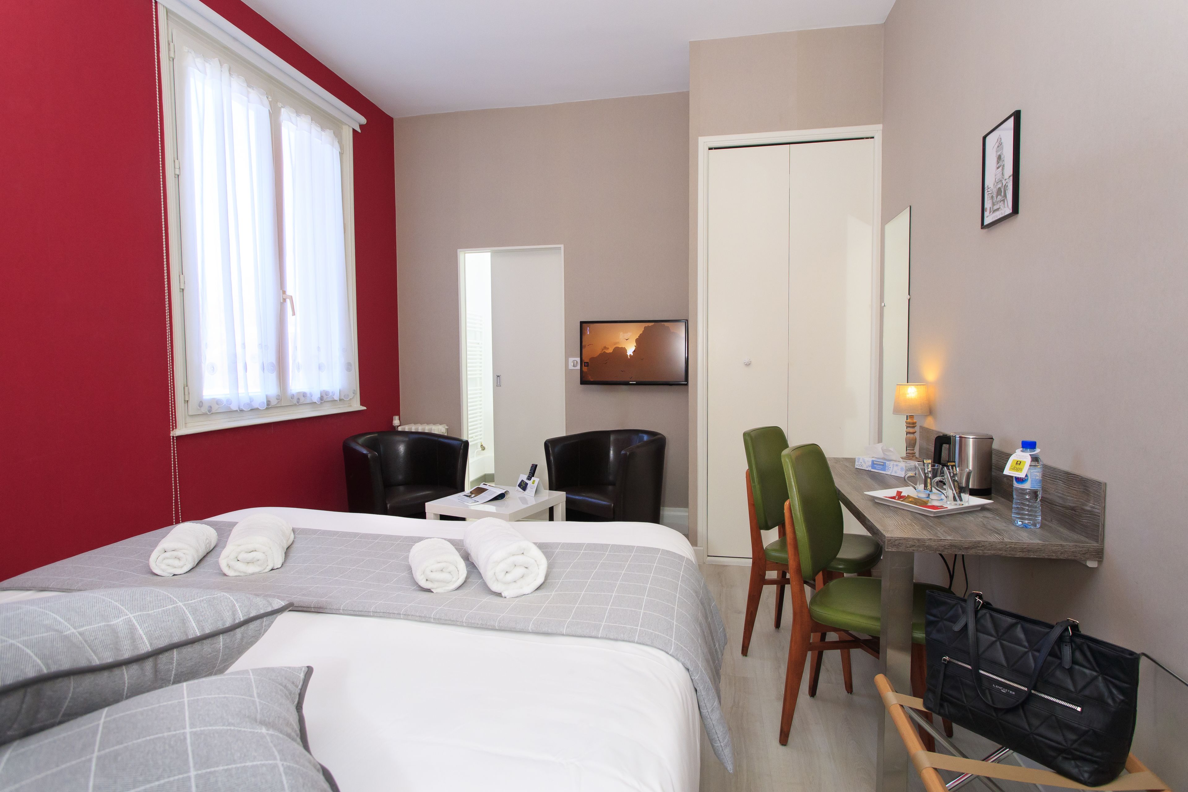 A hotel room with a bed, a desk, a chair, a TV, and a wardrobe.