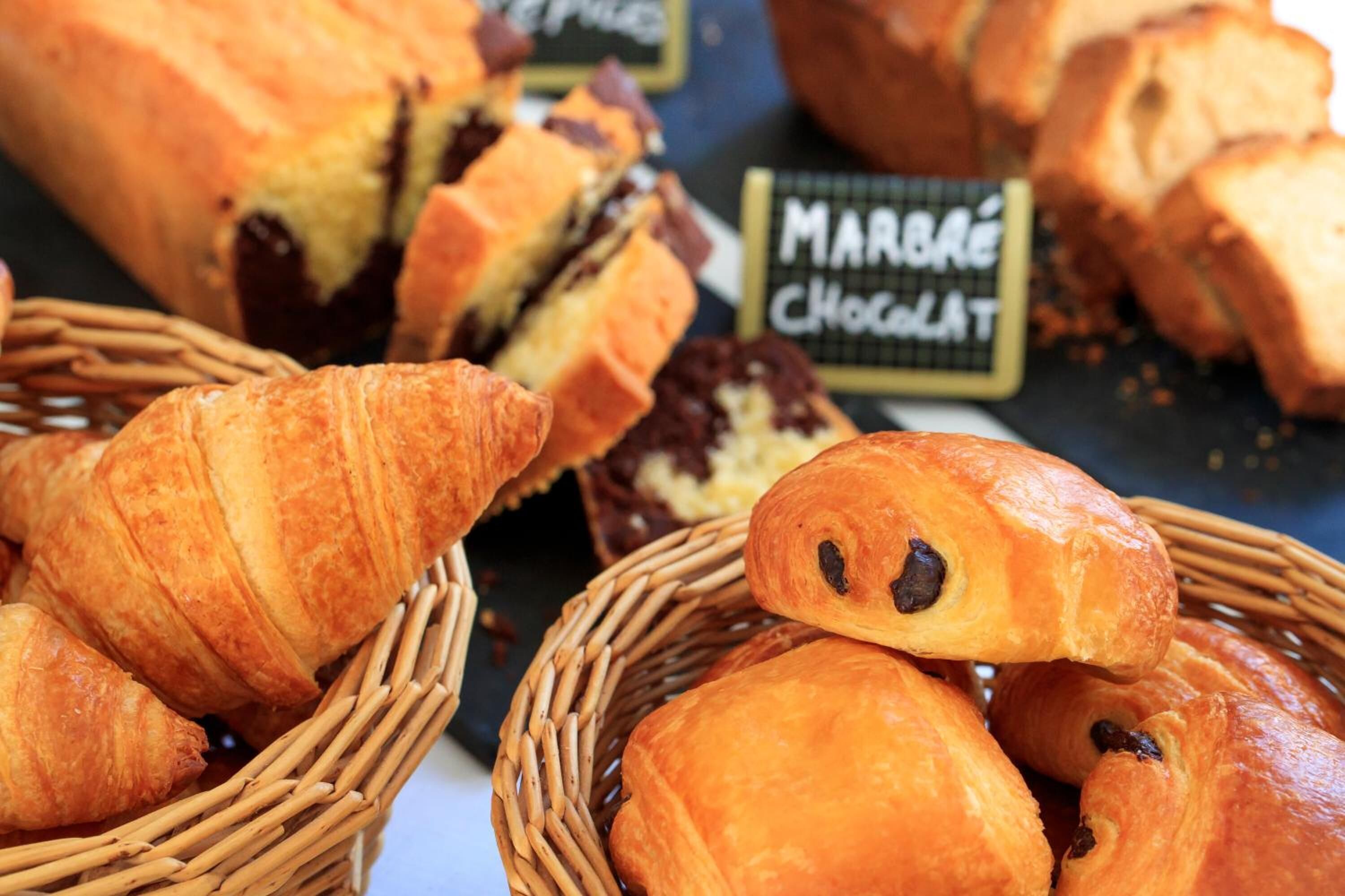 Diversitat de pastissos, incloent croissants i pa de xocolata, exposats en cistos de vimet.