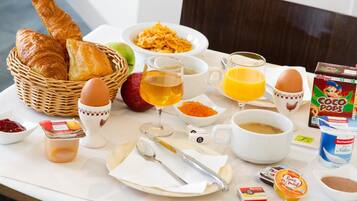 Una mesa de desayuno con cruasanes, cereal, fruta, café, jugo y varias salsas.