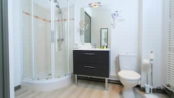A modern bathroom with a glass shower enclosure, a white toilet, a dark-colored vanity with two drawers, and a mirror above the sink.