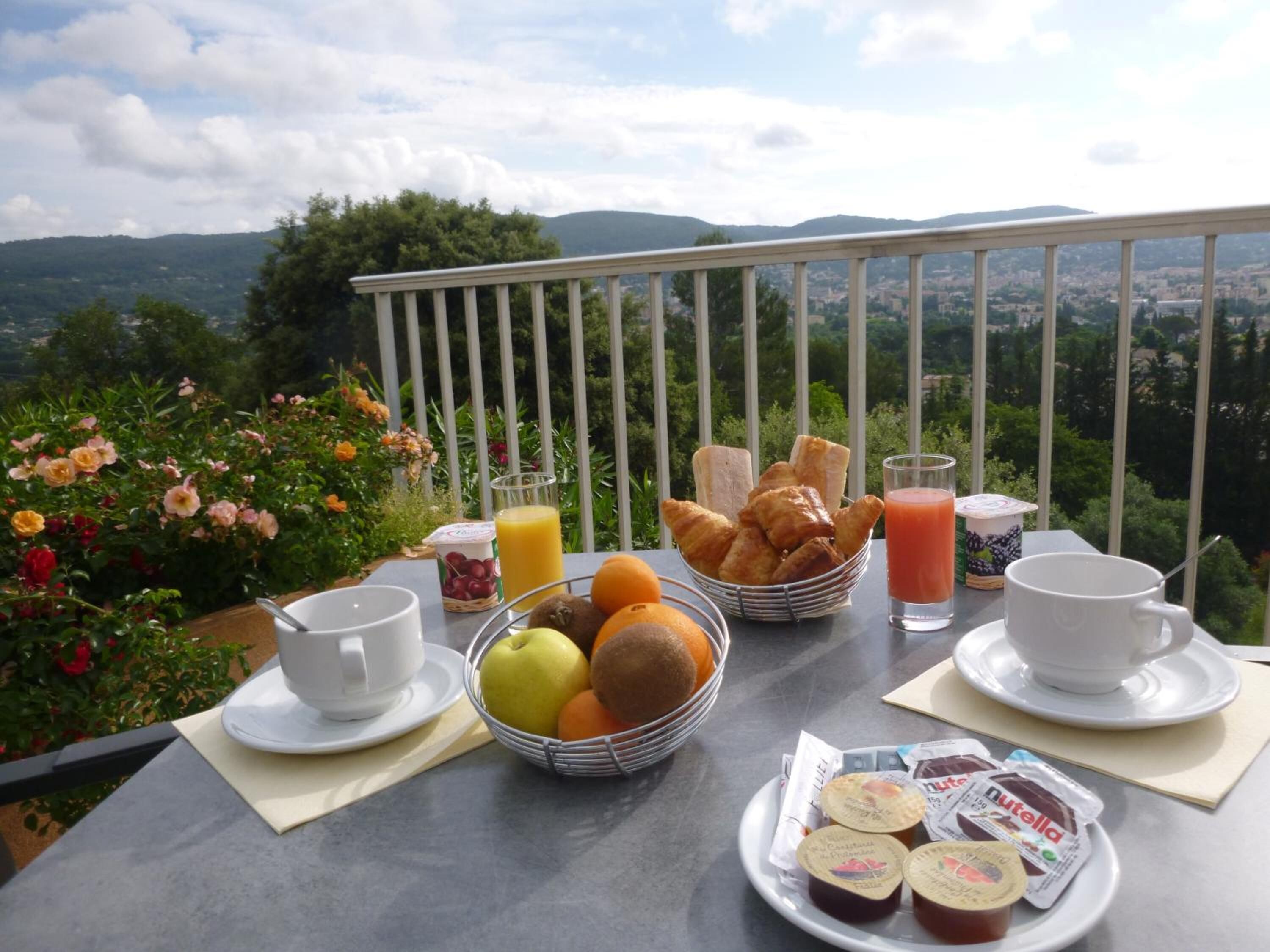 Desayuno con cruasanes, frutas, jugo y Nutella en un balcón con vistas a un paisaje pintoresco.