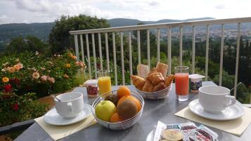 Desayuno con cruasanes, frutas, jugo y Nutella en un balcón con vistas a un paisaje pintoresco.