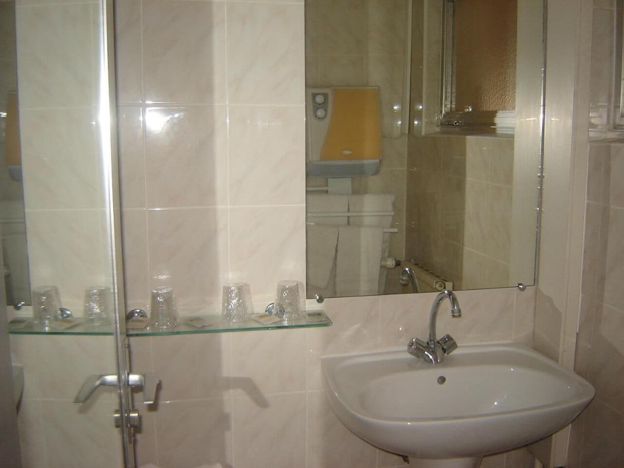 Bany amb prestatgeries de vidre que sostenen productes de tocador, un lavabo blanc i un mirall.
