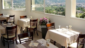 A restaurant with multiple tables and chairs, large windows offering a view of a mountainous landscape.