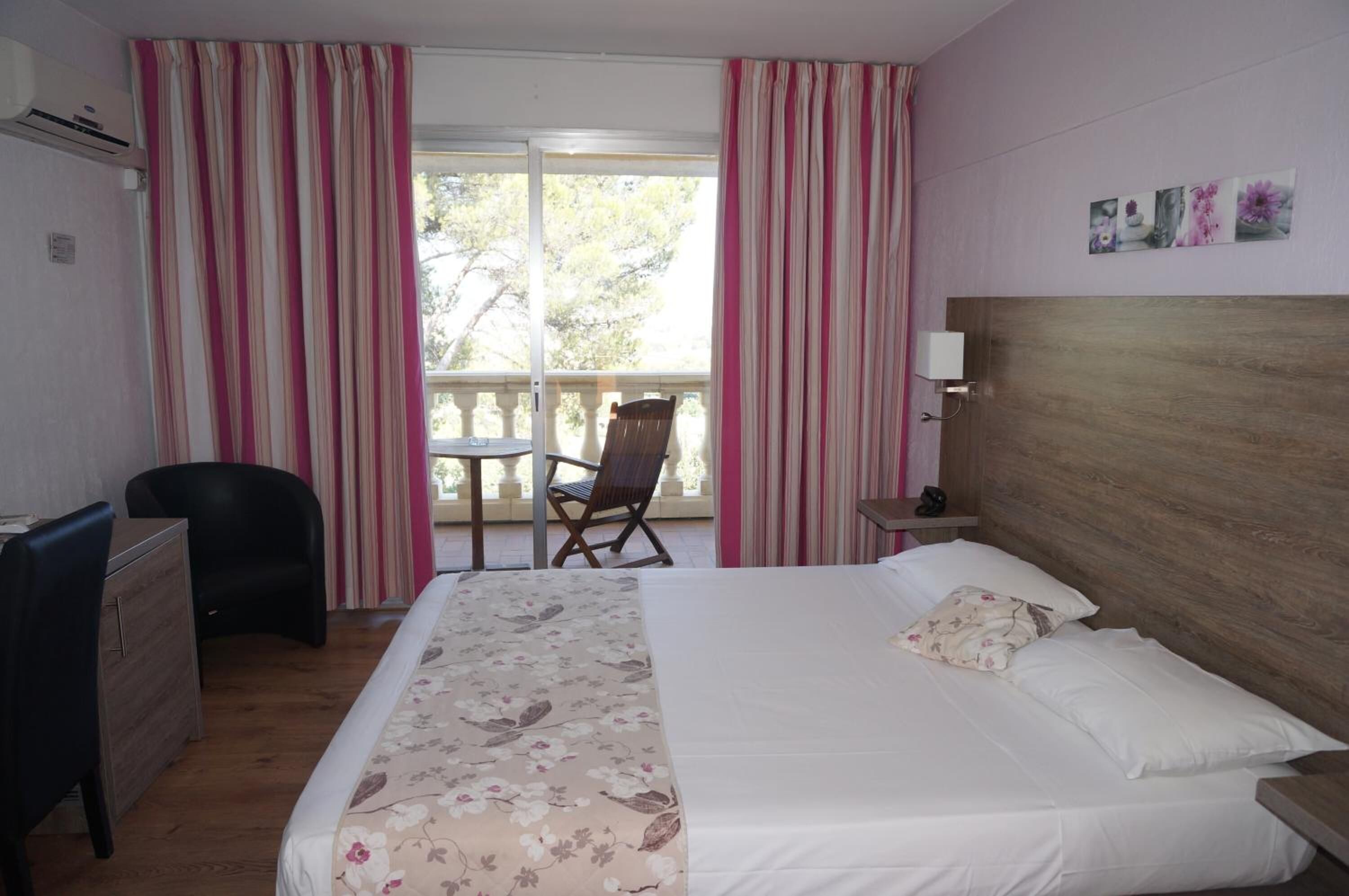 Une chambre d’hôtel avec un lit, un bureau, une chaise et un balcon avec des rideaux.