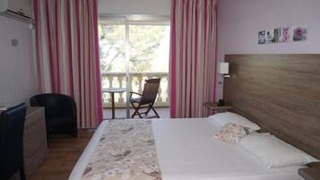 Une chambre d’hôtel avec un lit, un bureau, une chaise et un balcon avec des rideaux.