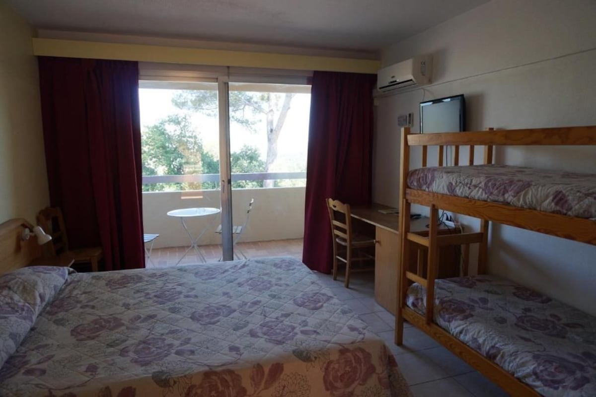 A room with a bed, a desk, a bunk bed, a chair, a small table, and a window with curtains.