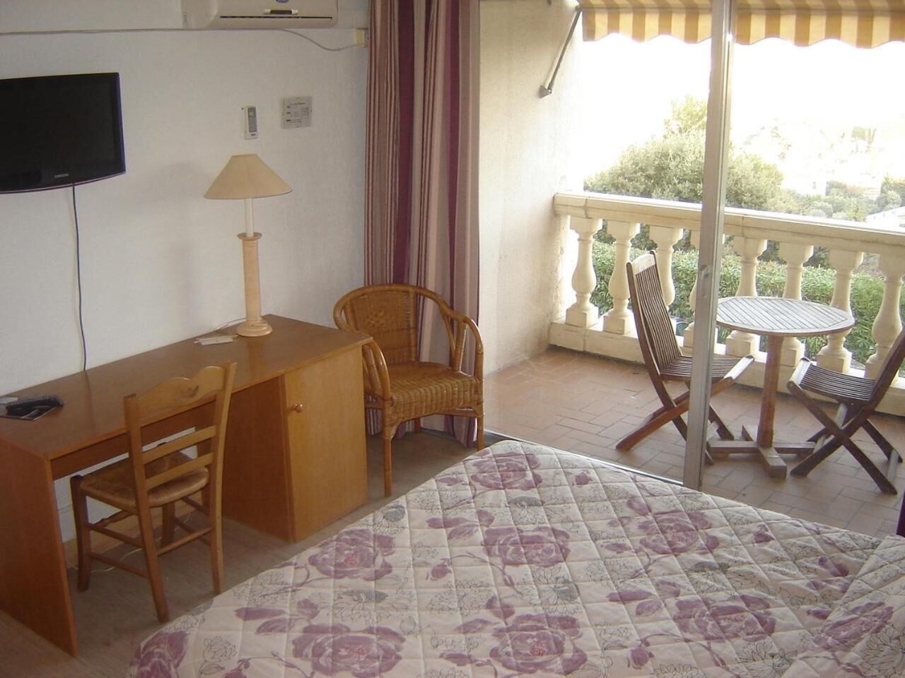 A room with a bed, a desk, a chair, a table, and a balcony with chairs.