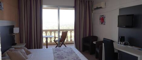 A hotel room with a bed, a desk, a chair, a TV, and a balcony with curtains.
