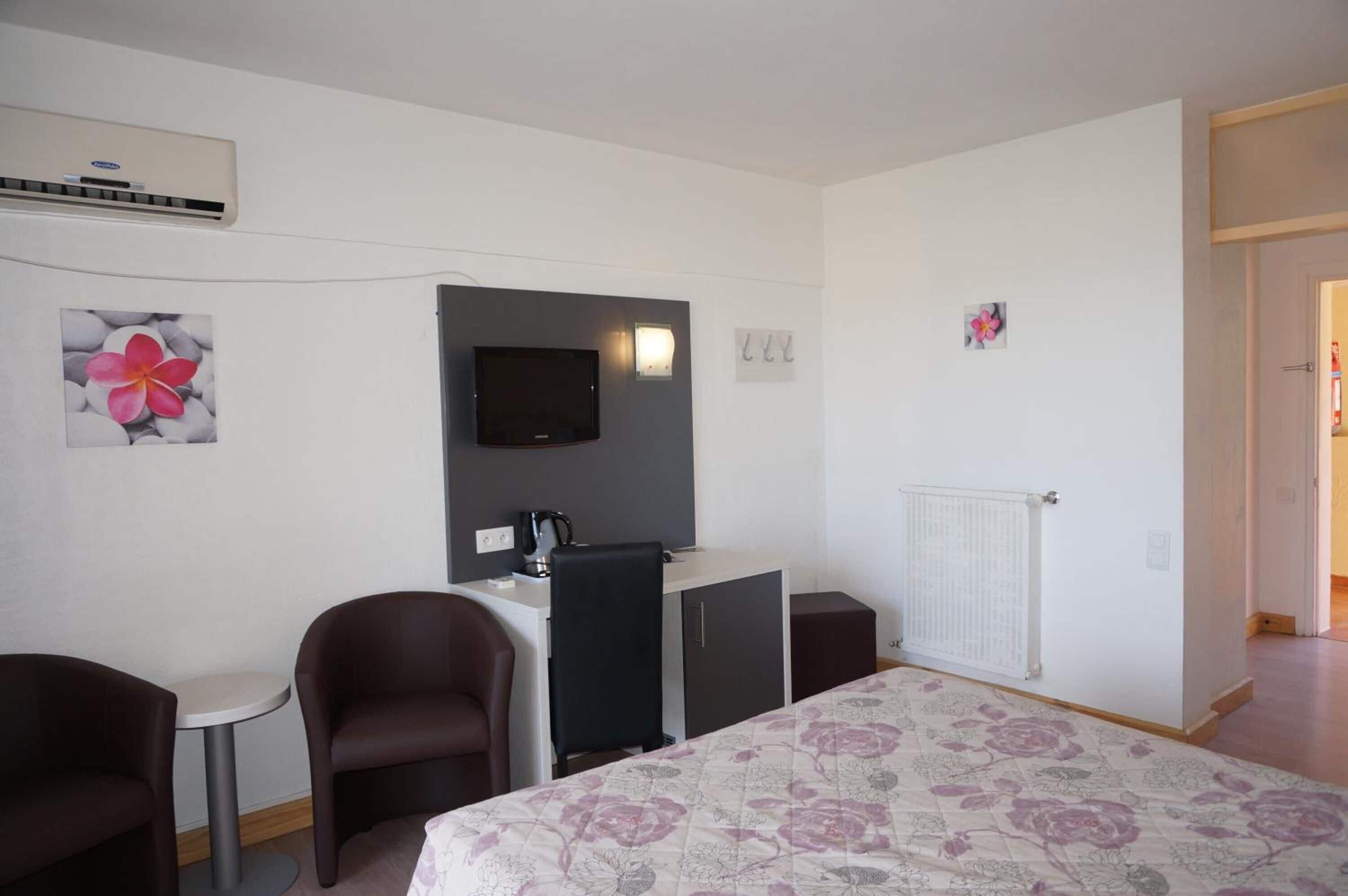 Ein Hotelzimmer mit Bett, Schreibtisch, zwei Stühlen, Fernseher und Heizkörper.