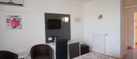 A hotel room with a bed, a desk, two chairs, a TV, and a radiator.
