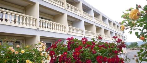 Un hôtel à plusieurs étages, doté de balcons et d’un jardin agrémenté de fleurs rouges et jaunes.