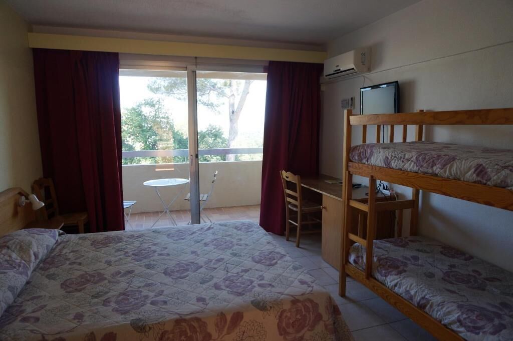 A room with a bed, a desk, a bunk bed, a chair, a small table, and a window with curtains.