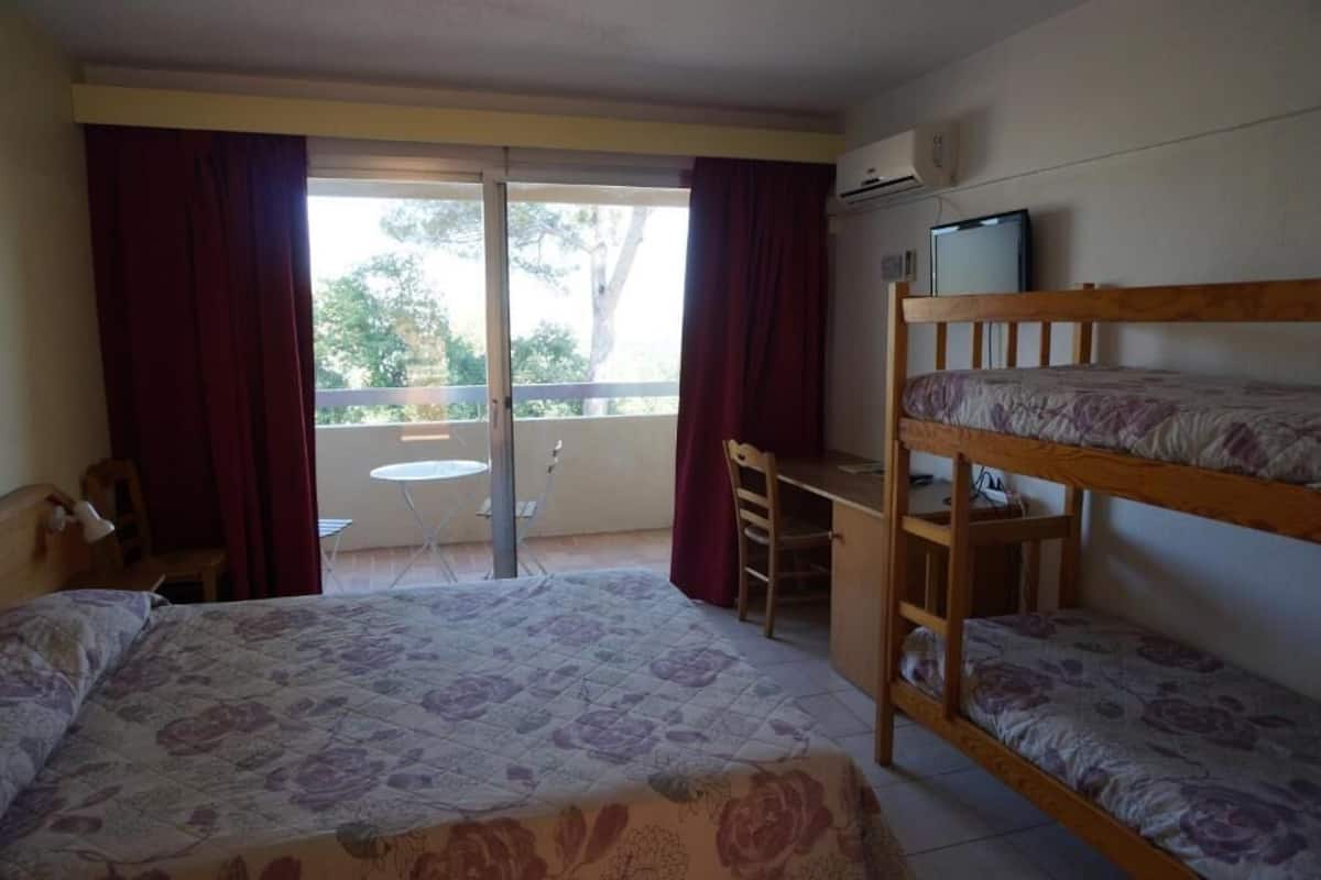 Quarto com cama, escrivaninha, beliche, cadeira, mesa pequena e janela com cortinas.