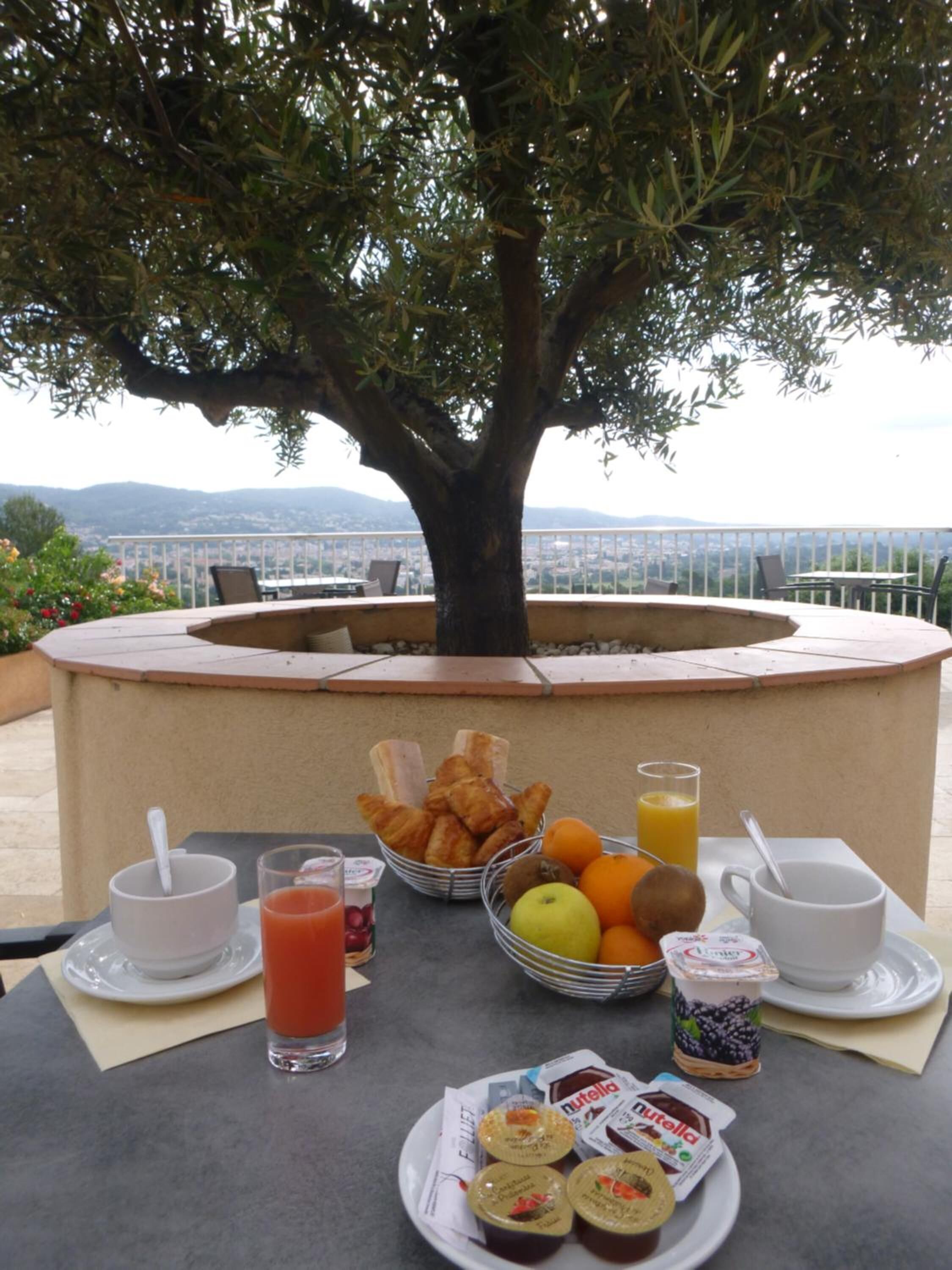 Desayuno con cruasanes, frutas, jugo y Nutella en una terraza con vistas al mar y a las montañas.