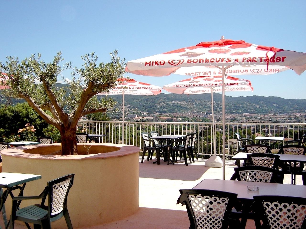An outdoor terrace with tables and chairs, umbrellas, and a view of the city.