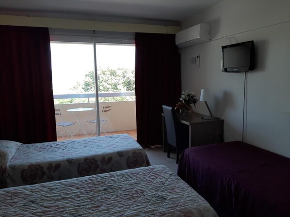 Habitación de hotel con dos camas, un escritorio con silla, televisión y balcón con mesa y sillas.