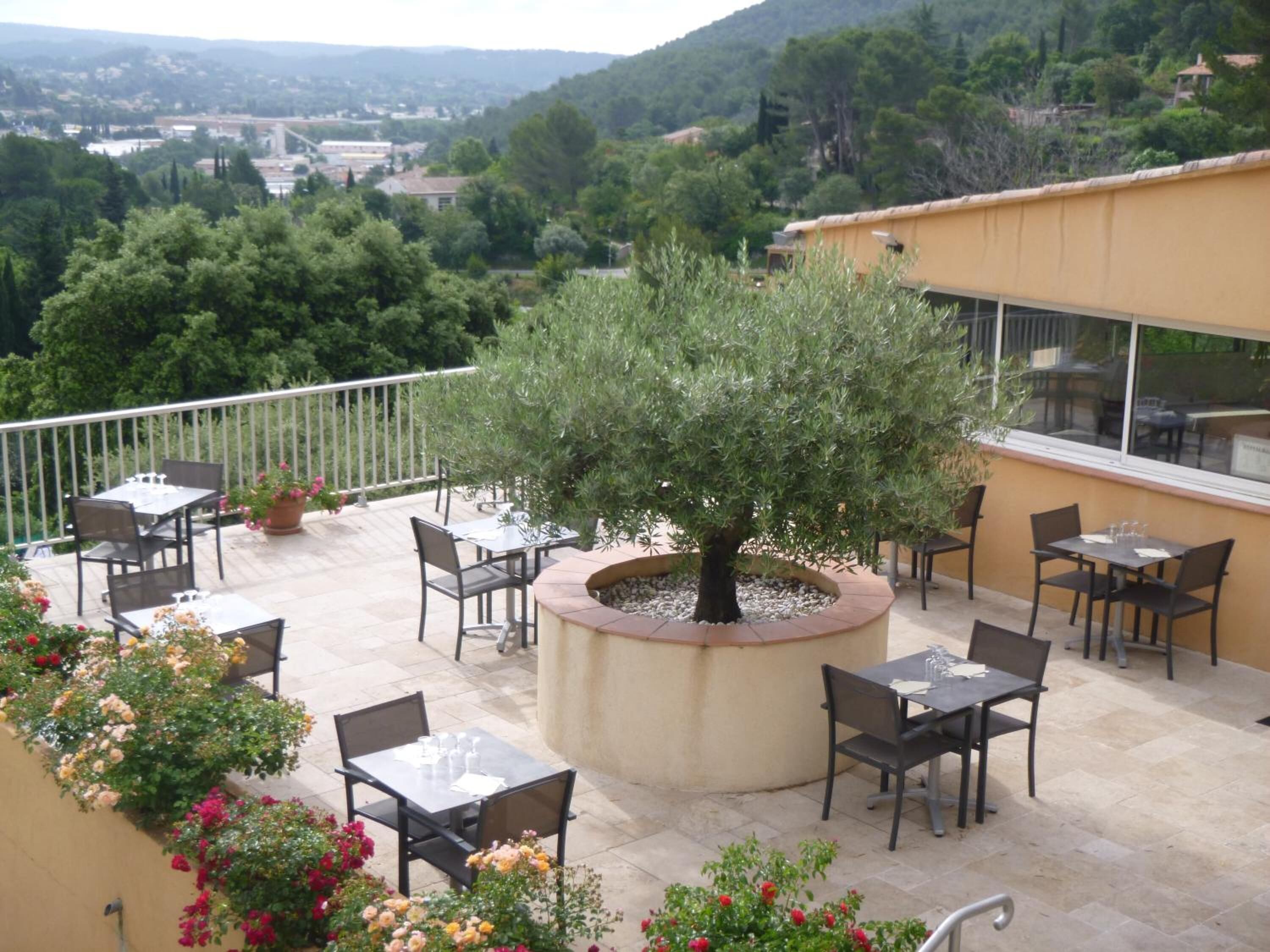 A terrace with outdoor seating, a central tree planter, and a view of a hilly landscape.