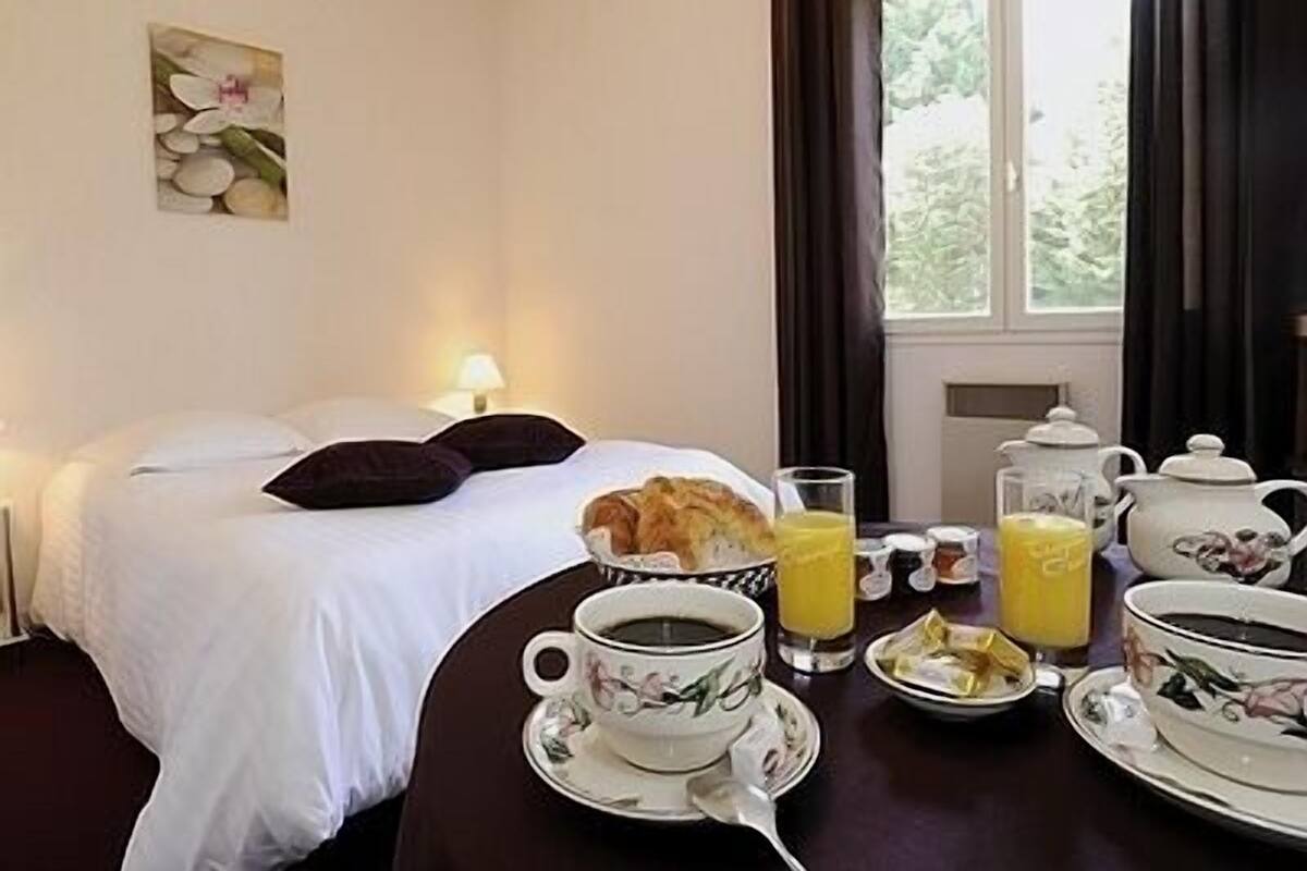 Una habitación de hotel con cama, una mesa con alimentos para el desayuno y una ventana con cortinas.