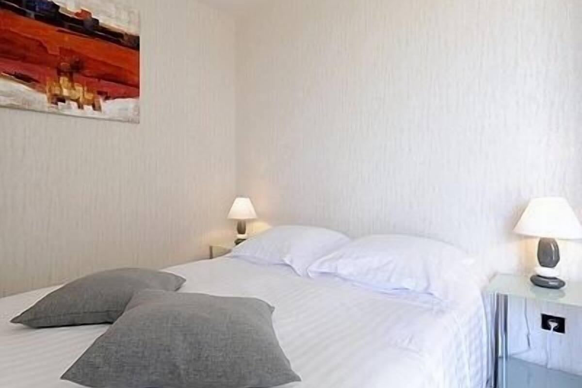 Una habitación de hotel con una cama, dos almohadas, una mesita de noche con una lámpara y un cuadro en la pared.
