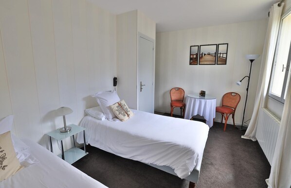 A hotel room with a bed, a small table, two chairs, a lamp, and a door. - Hotel Des Grands Vins (Fleurie)