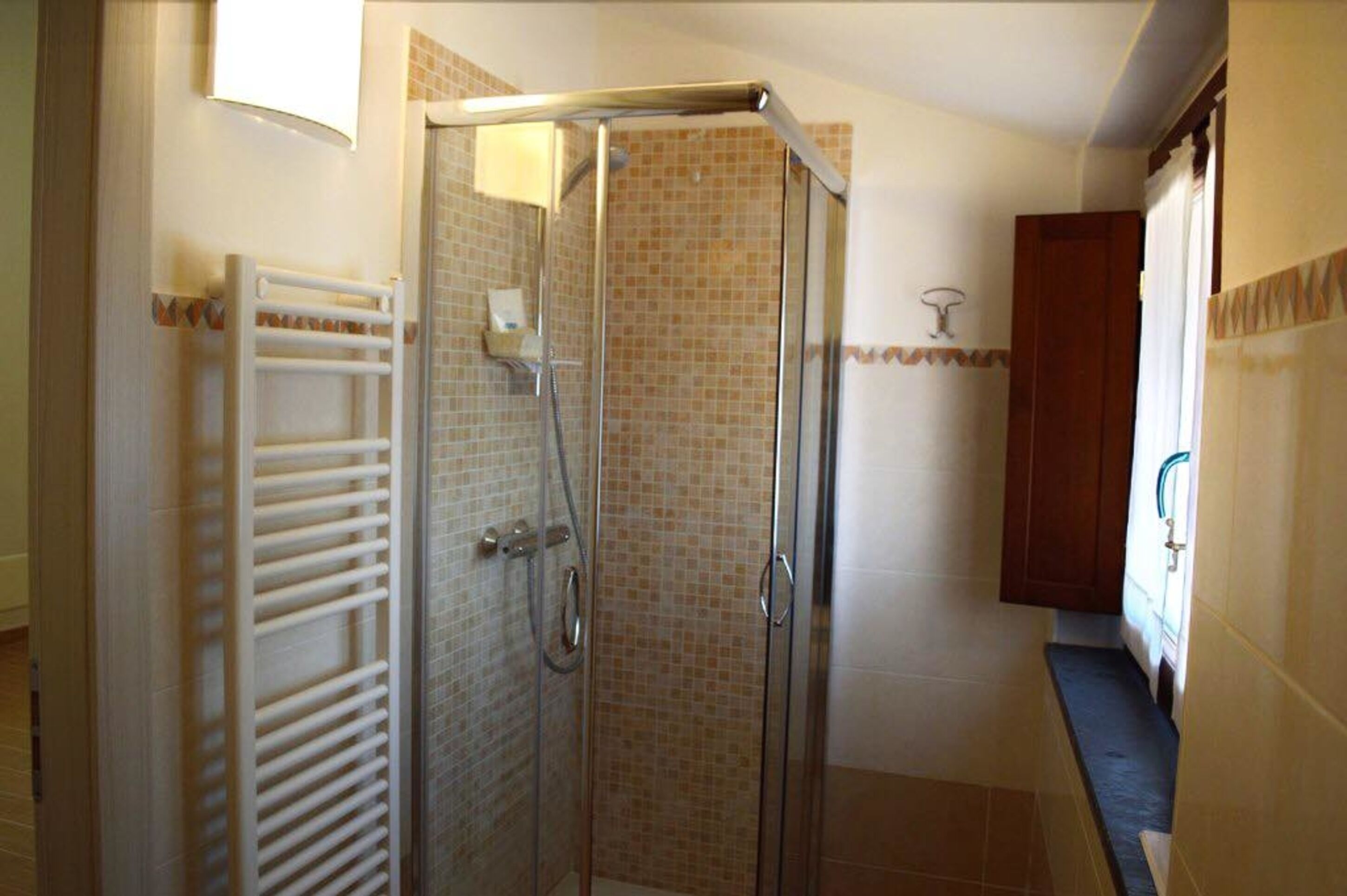A glass-enclosed shower with a tiled wall, a white towel rack, and a wooden cabinet.