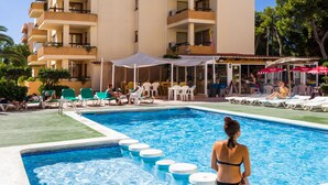 Ett hotell med en swimmingpool, solstolar och en möblerad uteplats under tak.