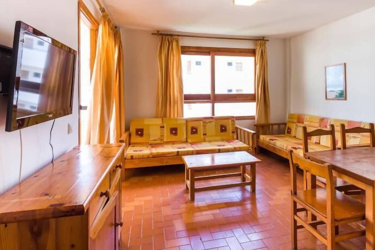 Una habitació acollidora amb un sofà, una taula de fusta i un televisor penjat a la paret.