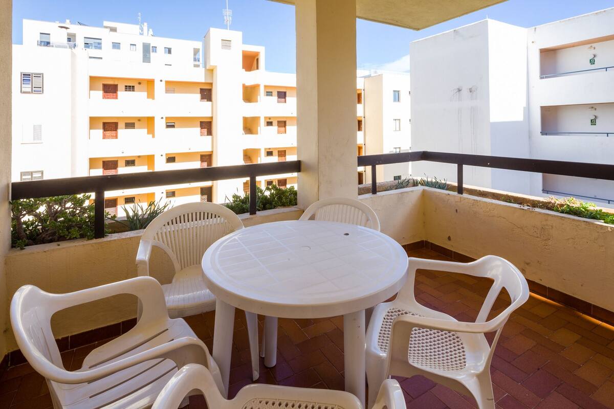 Un balcó amb una taula rodona i quatre cadires de plàstic blanc, amb vista a una fila d'edificis blancs amb balcons.