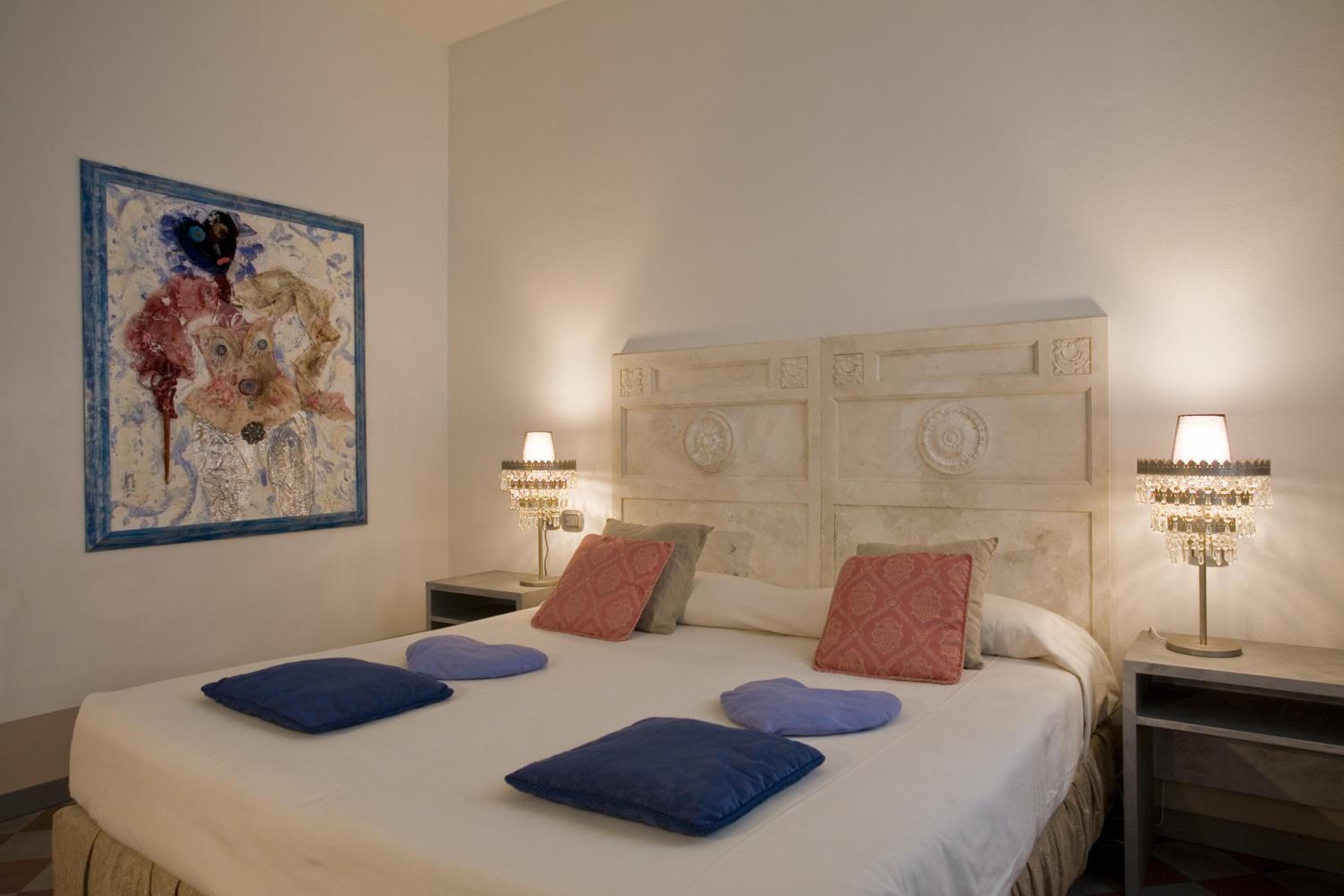 A hotel room with a large bed, two bedside lamps, a decorative headboard, and a piece of abstract art on the wall.