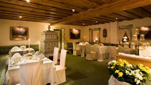 A dining area with wooden ceilings, green upholstered benches, and tables set for a meal. - Hotel Sassongher – Preferred Hotels & Resorts (Corvara in Badia)