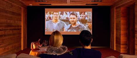 A cozy room with a wooden ceiling and walls, a large screen for watching movies, and a comfortable seating area.