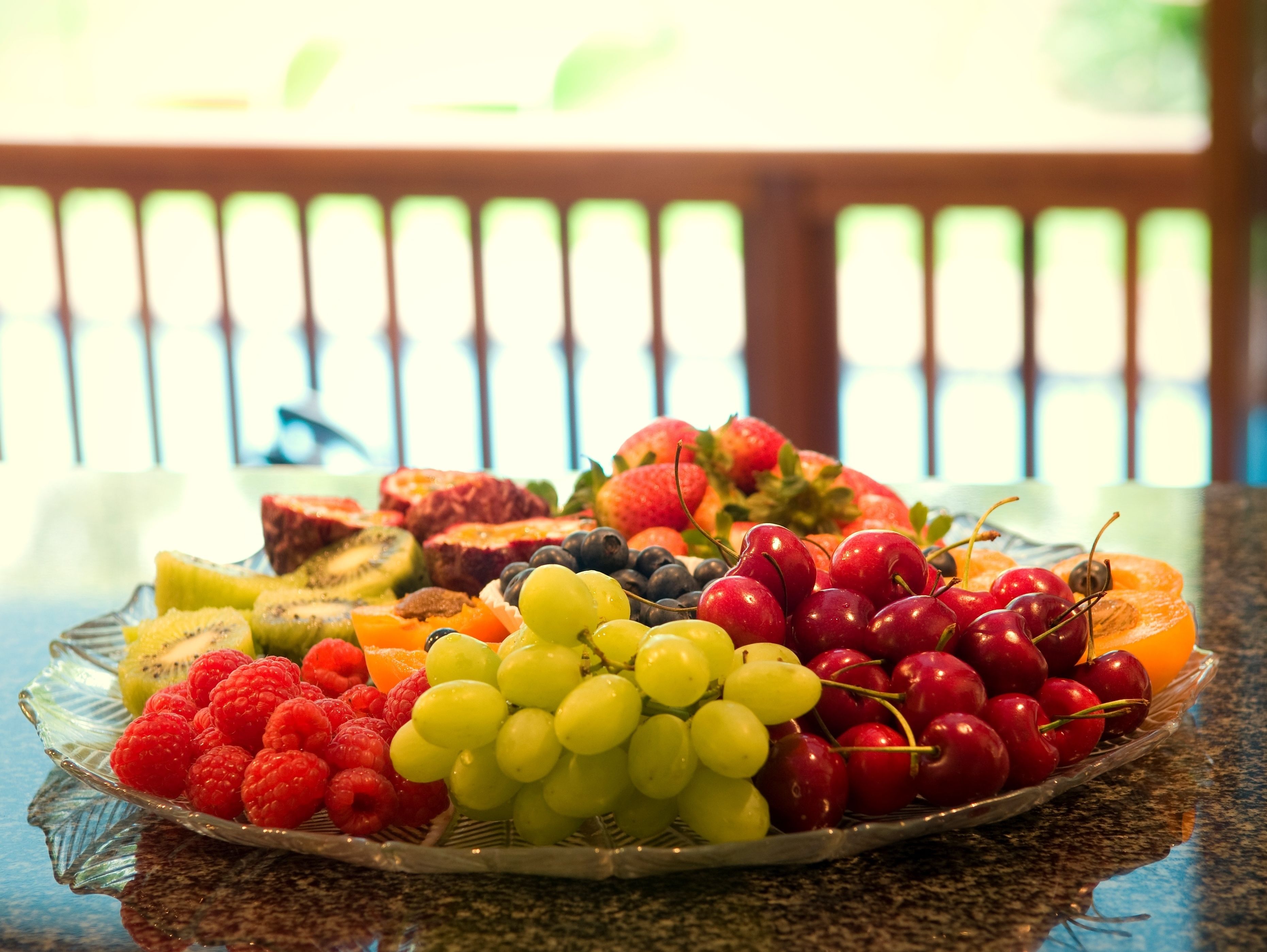 Una bandeja de fruta sobre una mesa de vidrio, con un fondo exterior desenfocado.