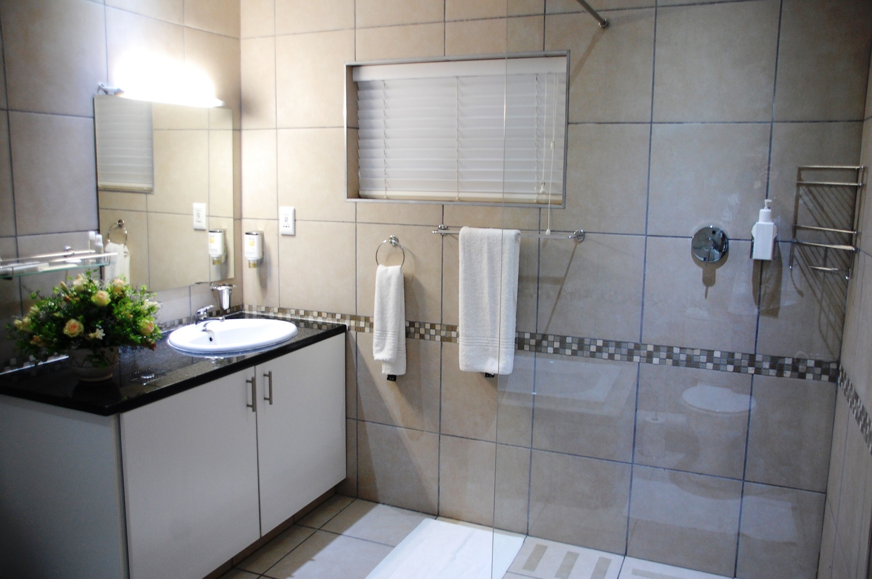 A bathroom with a sink, mirror, towel rack, and shower area.