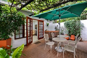 A patio with a table and chairs, a green umbrella, and potted plants.