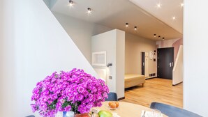 A modern room with a dining table, a vase of purple flowers, and a bed in the background.