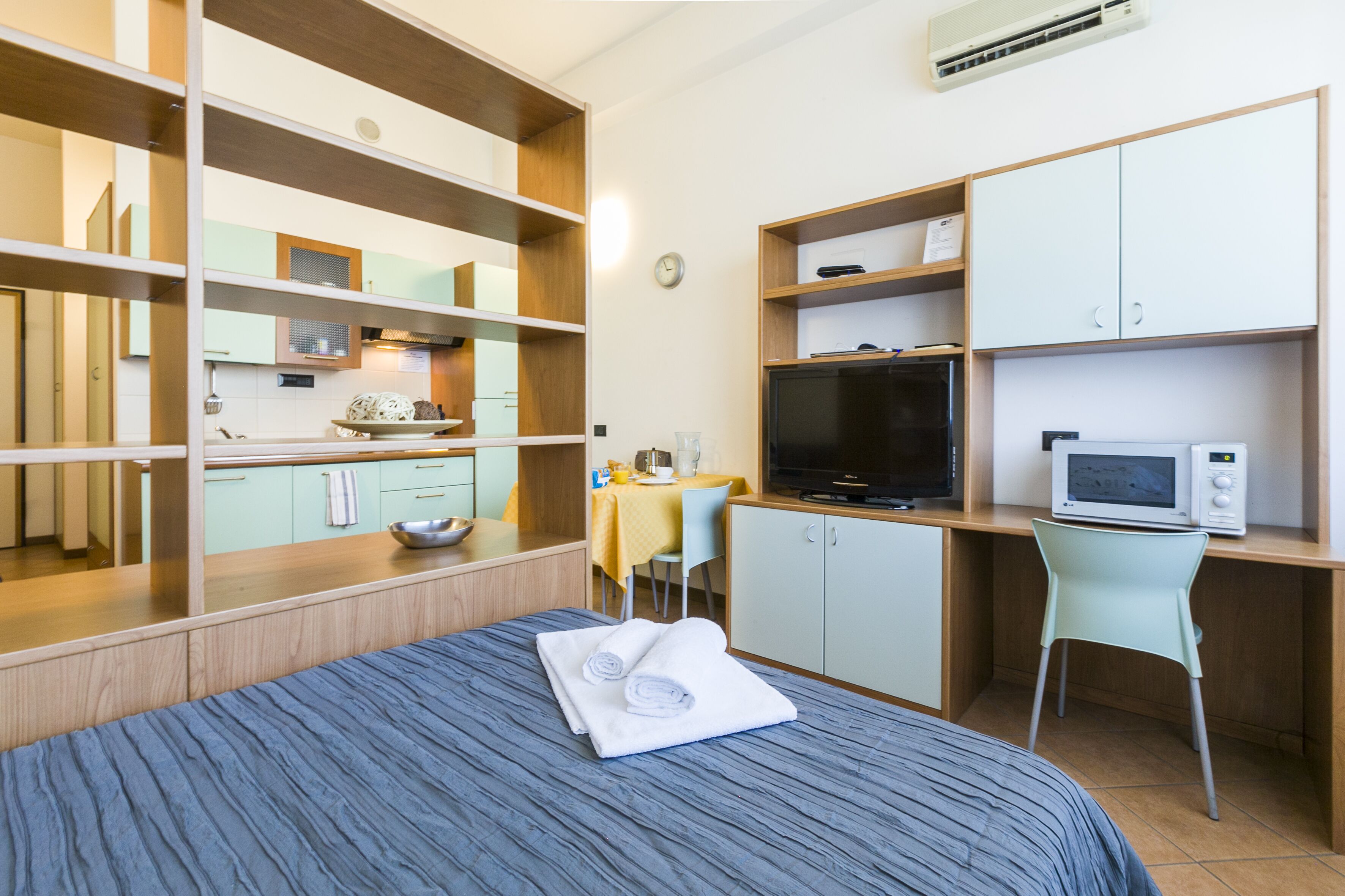 Una habitación de hotel con cama, escritorio con computadora, televisor y kitchenette.