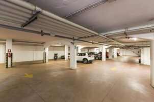 Un aparcamiento de varios niveles con varios coches estacionados, columnas estructurales visibles y flechas direccionales en el suelo.