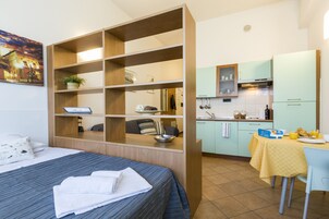 Una camera d'albergo compatta con un letto, una scrivania integrata, un angolo cottura e un'area ristoro.