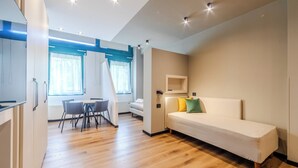 A modern, well-lit room with a bed, a dining table with chairs, and a small kitchenette area.