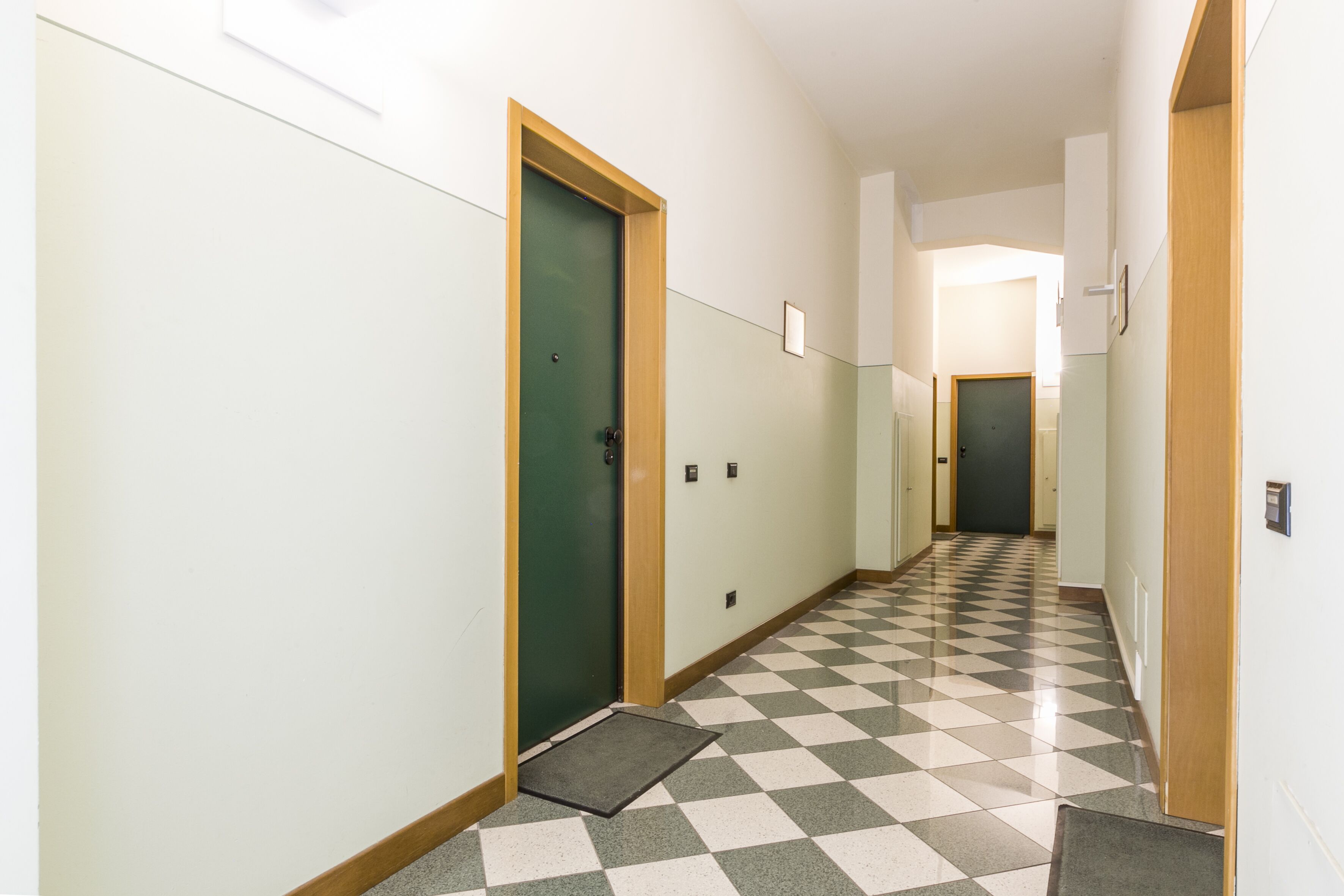 Un couloir doté d’un sol à carreaux, d’une porte verte et d’un cadre de porte en bois.