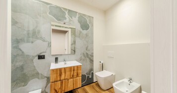 Een badkamer met een houten wastafelmeubel, een witte wastafel, een spiegel, een toilet en een bidet.