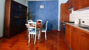 Une cuisine de taille réduite avec des meubles en bois, une table à manger avec des chaises et un mur d’accent bleu.