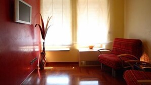 Une pièce avec un mur rouge, une fenêtre ornée de rideaux légers, une petite table, une chaise et une plante.
