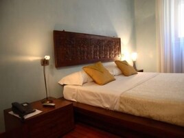 Quarto com cabeceira de madeira, mesa de cabeceira com abajur e duas almofadas.