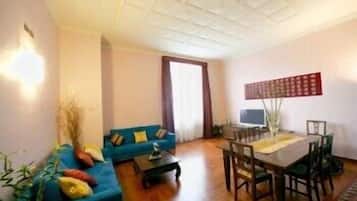 Una sala de estar con un sofá azul, una mesa de comedor con sillas, un televisor y un adorno en la pared.