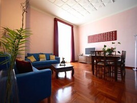 Uma sala de estar com um sofá azul, uma mesa de centro e um espaço de jantar com mesa e cadeiras.