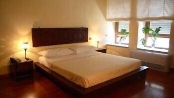 Una cama bien hecha en una habitación con cabecera de madera, una mesita de noche con lámpara y una ventana con vistas a zonas verdes.