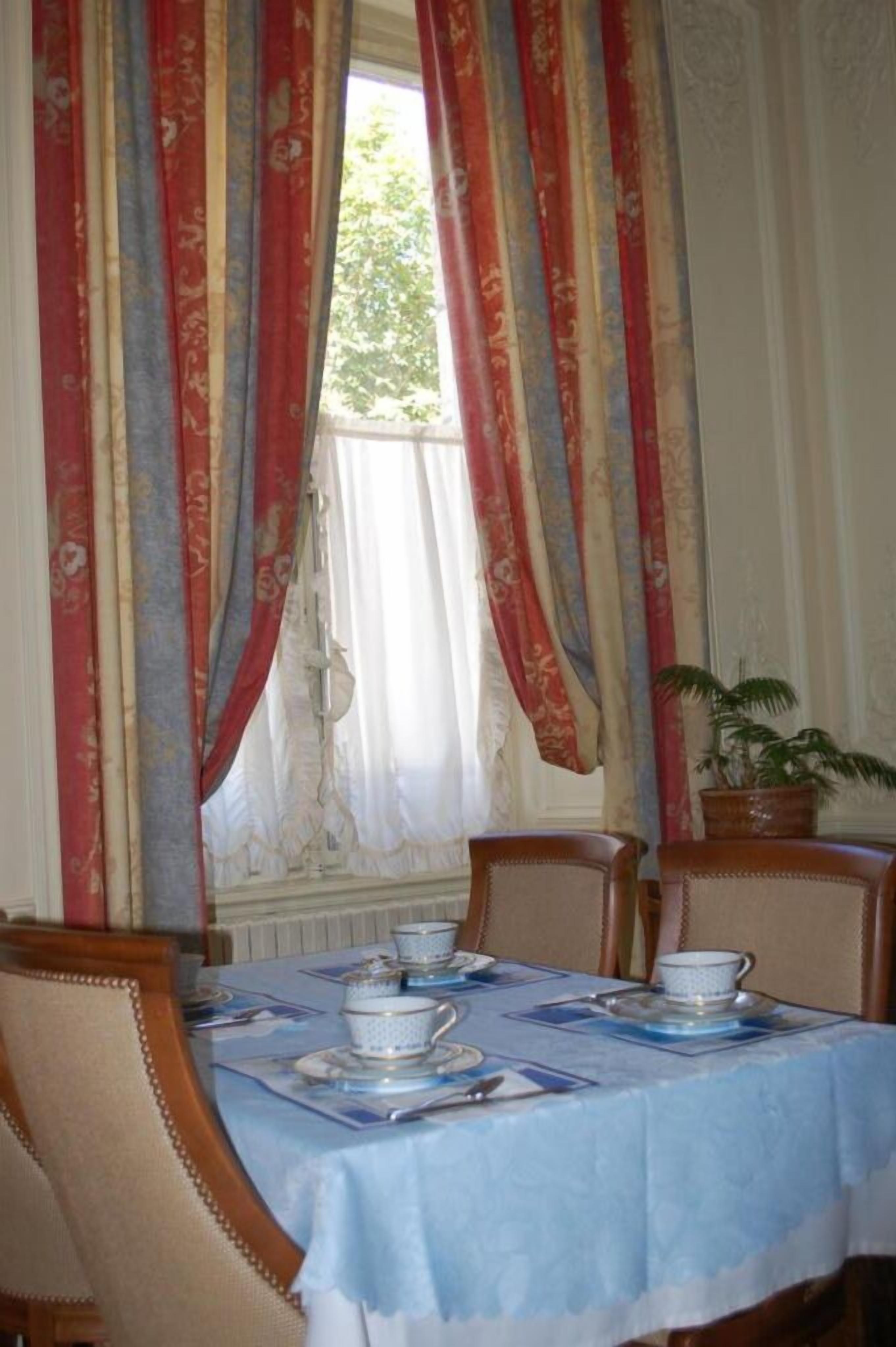 Un comedor con una mesa dispuesta para cuatro, cortinas y una planta en maceta.