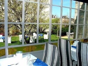 A dining area with a table set for two, chairs, and a view of a garden through large windows. - Hôtel de l'Europe (Pontivy)